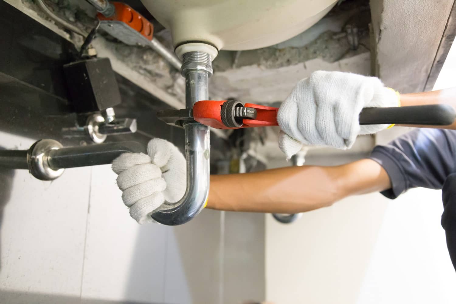 Plumber fixing white sink pipe with adjustable wrench.