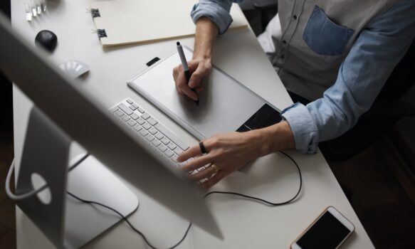 Designer hands using graphics tablet while working with computer at studio or office. Top side view.