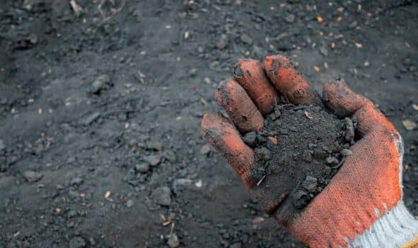 Testing the soil sample on hand which wears a glove with soil ground background. The concept of soil quality and farming