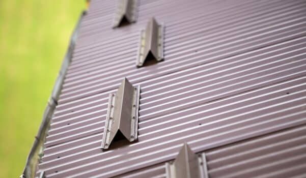 Close-up detail of metal brown shingle tiling house roof surface with rain gutter pipe and snow guards protective fence. Professional work, safety, construction, renovation and durability concept.