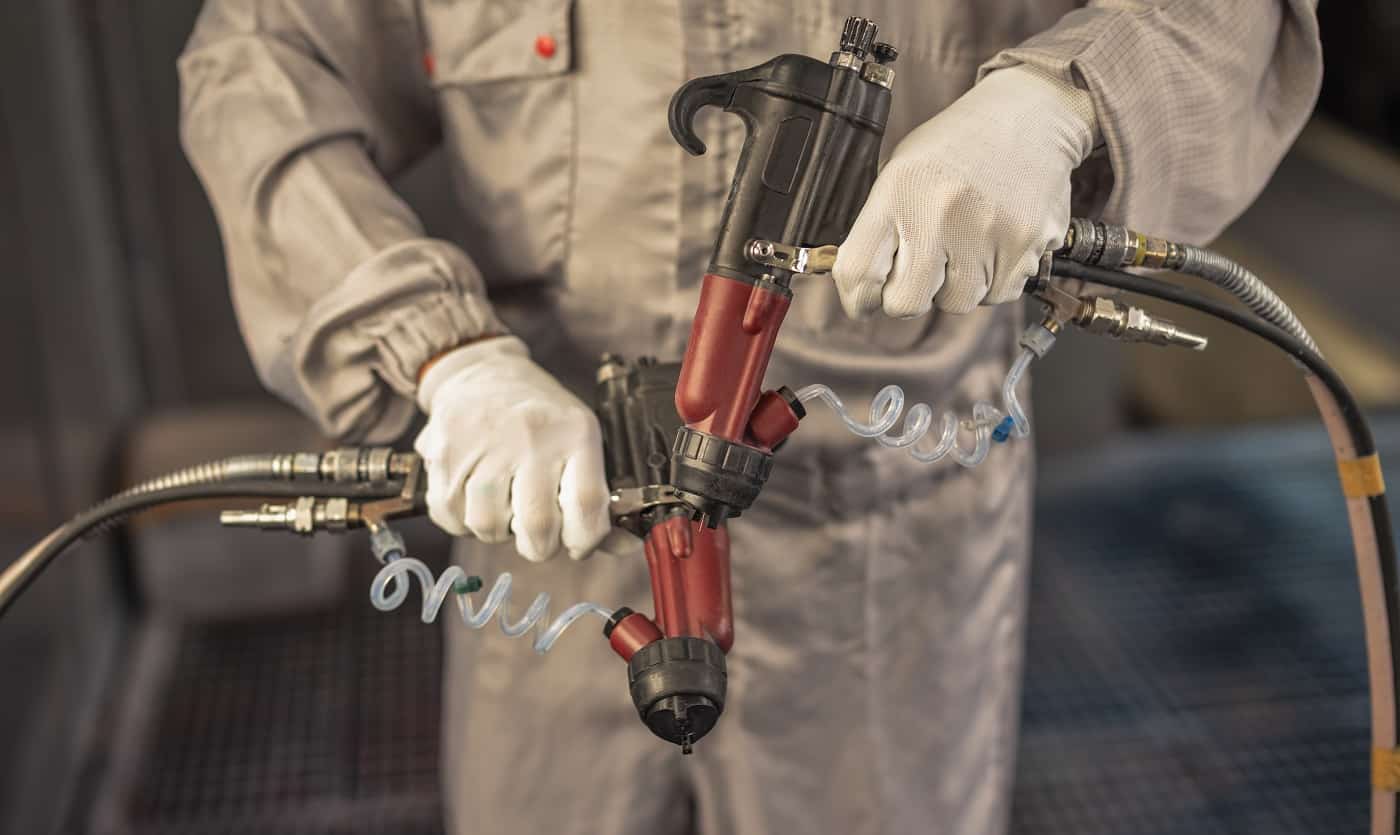 Paint shop worker with industrial sprayers in his hands, close-up