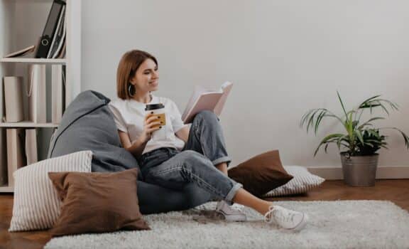 Short-haired girl in white t-shirt with smile reading book while sitting on soft bean bag