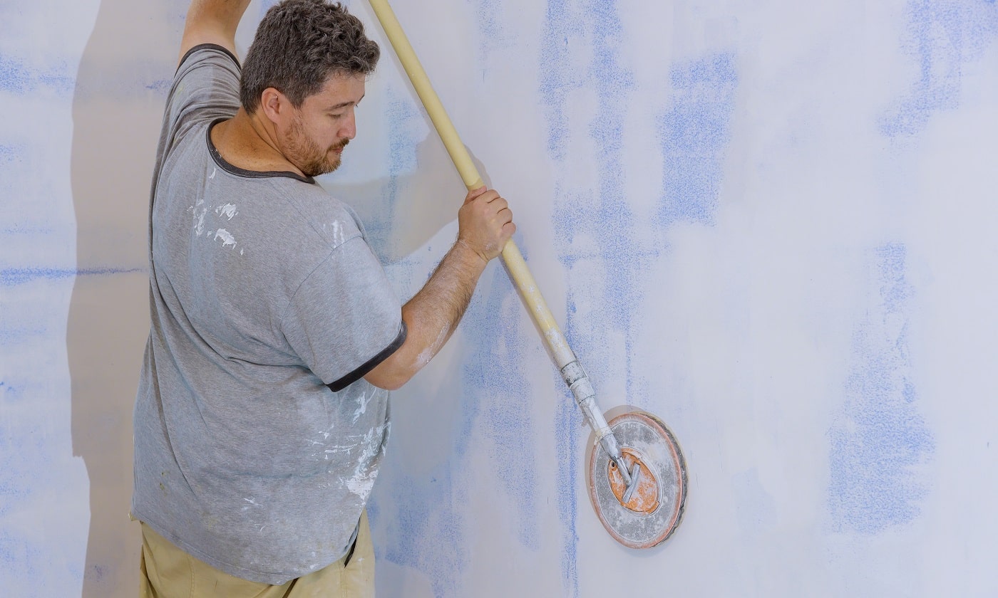 Contractor using sand trowel sanding the drywall on the wall