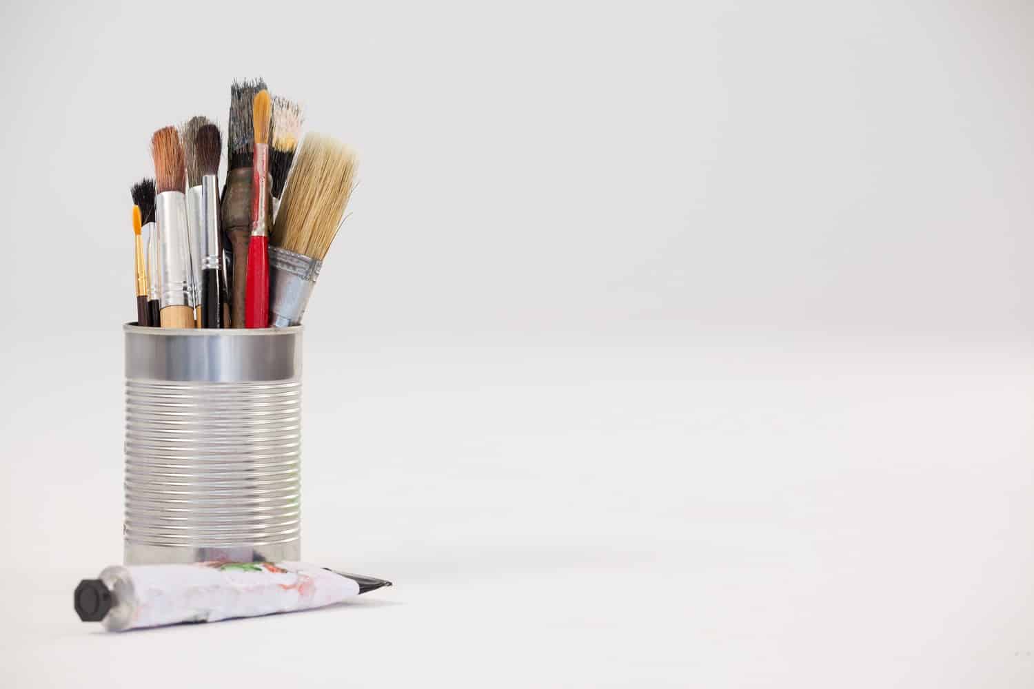 Varieties of paint brushes in metallic jar and tube color against white background