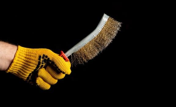 Close up hand of craftsman in a glove holds brush for removing rust