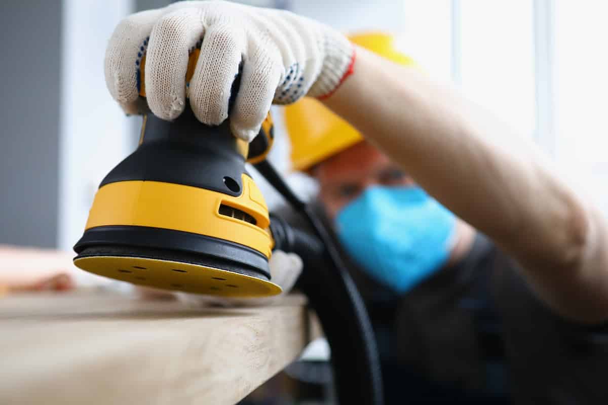 Close-up of man carpenter work with professional sander machine on flat project. Qualified worker polish wooden desk. Construction site sanding epoxy resin 101 [how to sand resin]