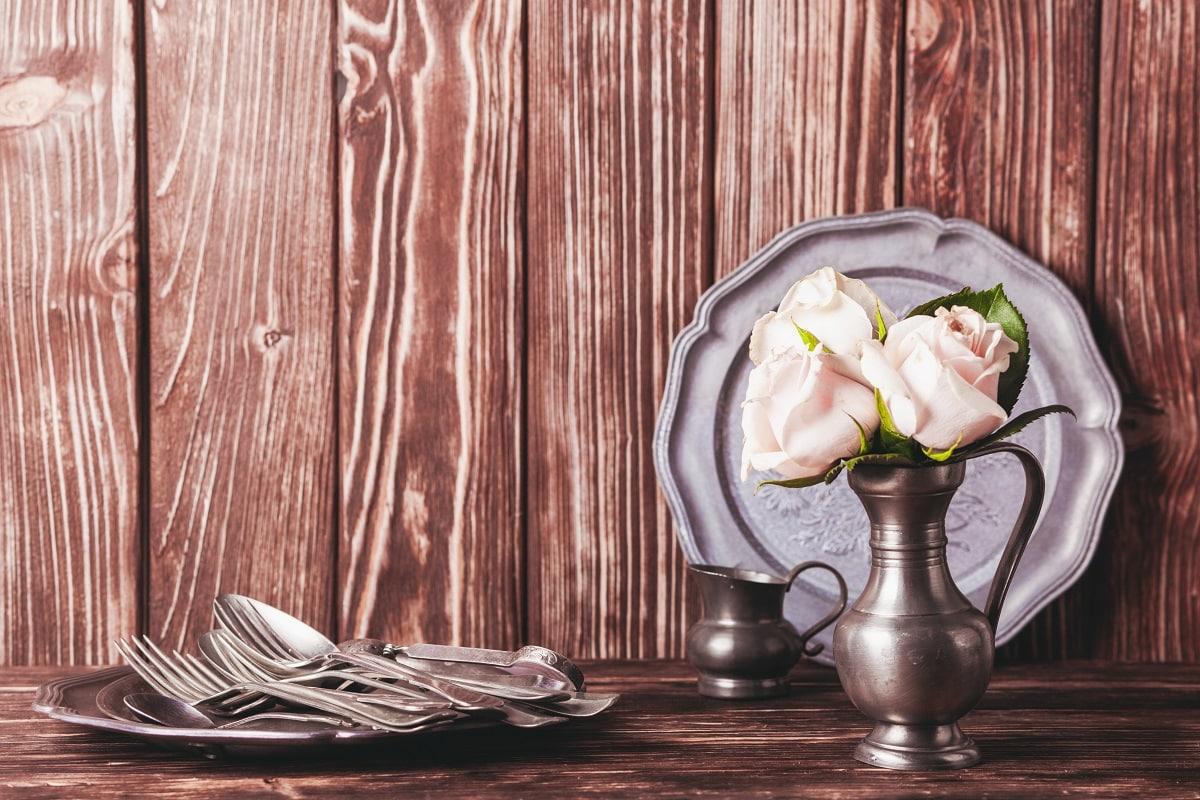 Still life with antique cutlery, plate and flowers in tin jug