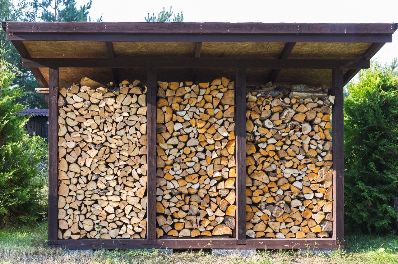 They prepare firewood for heating in winter. Firewood is neatly stacked under the roof of the shed for heating. Firewood storage shed.